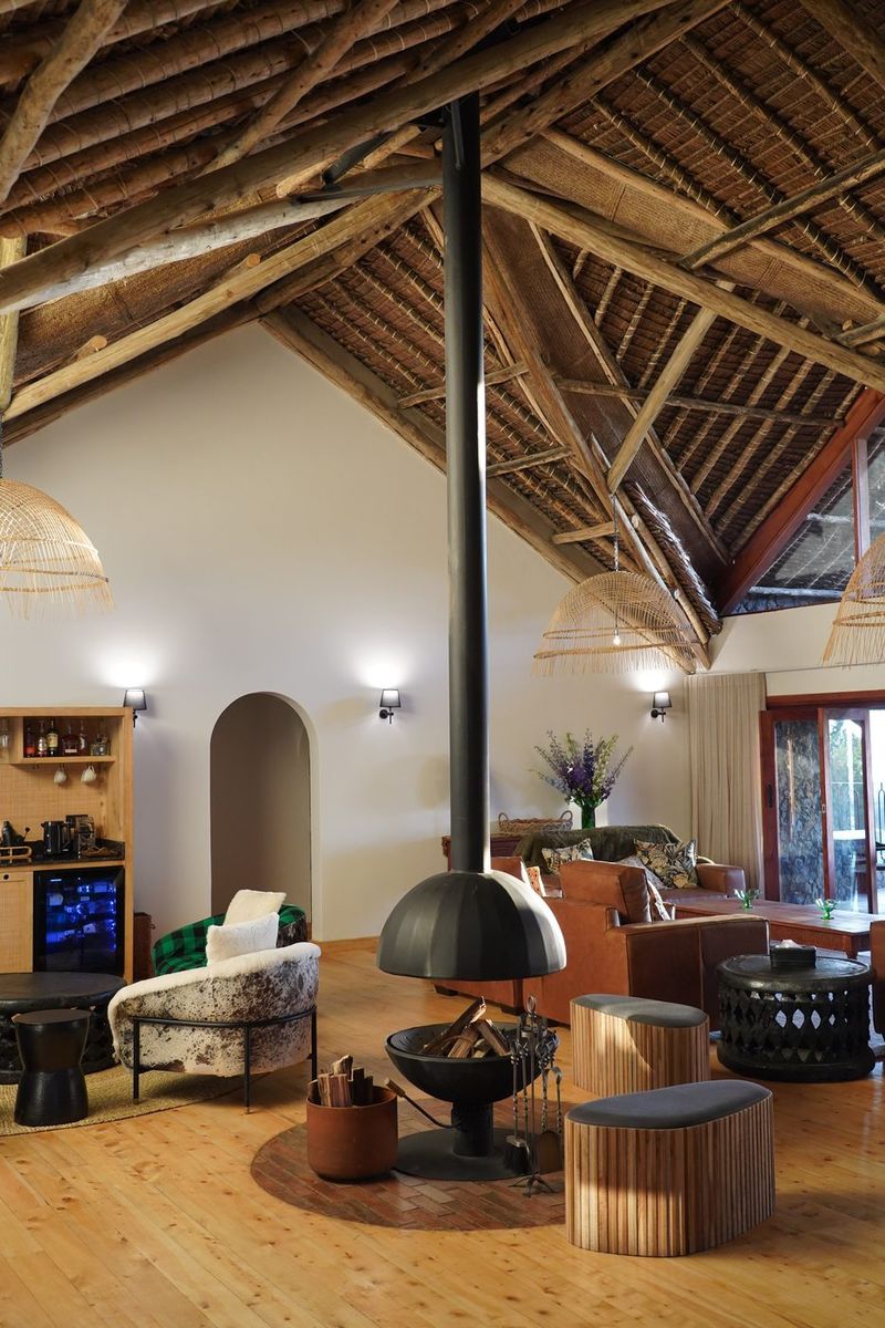 Looking up in the O'Leleshwa great room: the makuti thatch roof structure rising over the suspended black cone fireplace, bar and seating below.