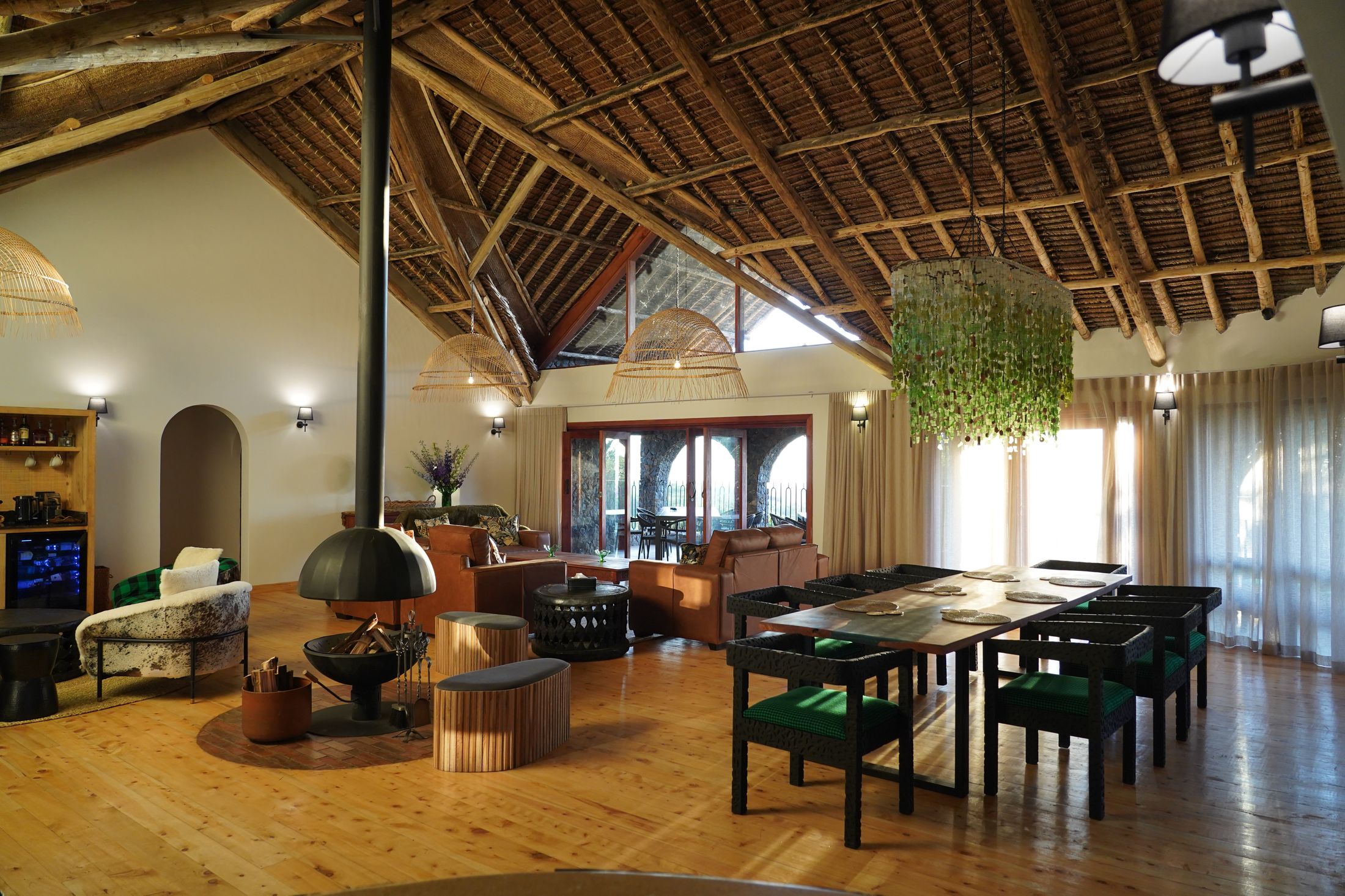 The O'Leleshwa great room — thatch vault, suspended cone fireplace, and the green glass-bead chandelier over the long dining table.