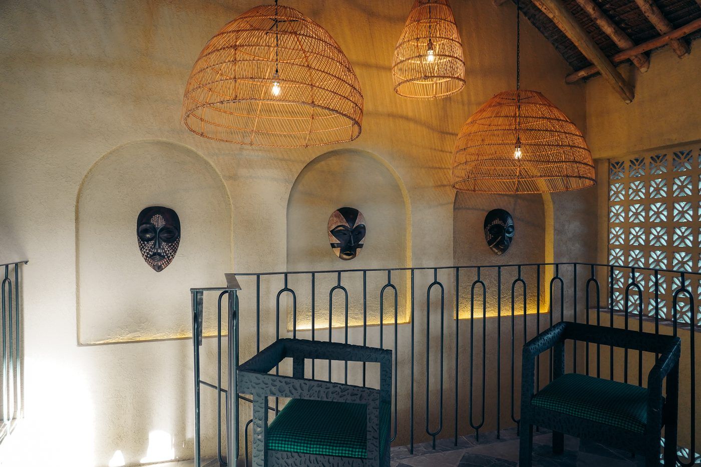 The mezzanine landing at O'Leleshwa: carved masks in underlit arched alcoves, rattan dome pendants and a wrought-iron balustrade.