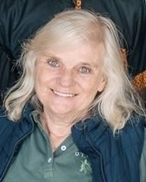 Jenetta Barry smiling, silver hair down, in a green polo shirt and navy gilet.