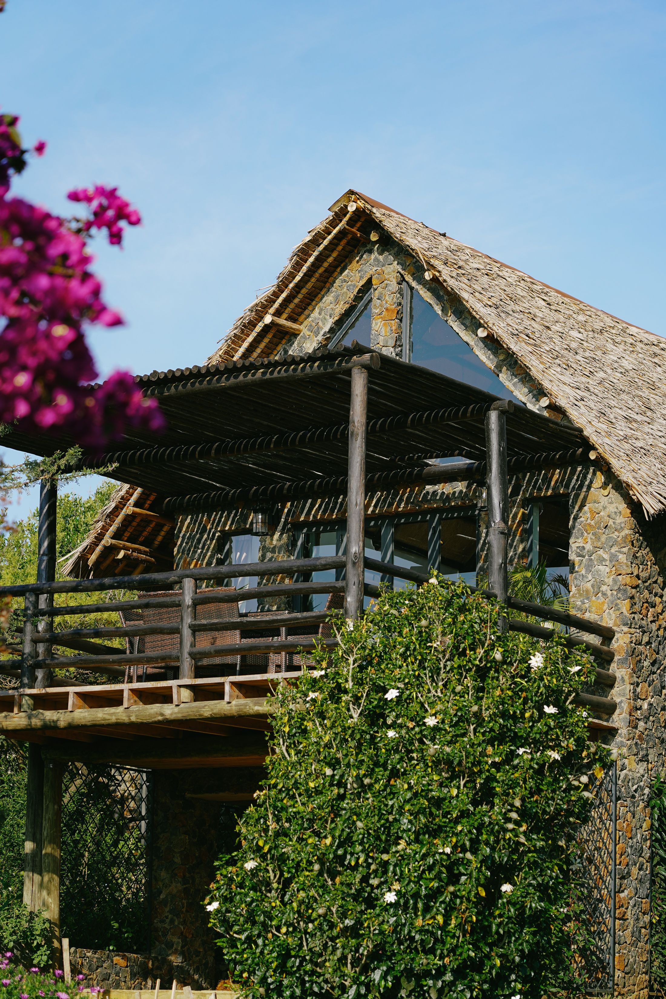O'Lorien's thatched A-frame with its triangular glass gable, seen past bougainvillea, the pole-pergola deck at its foot.
