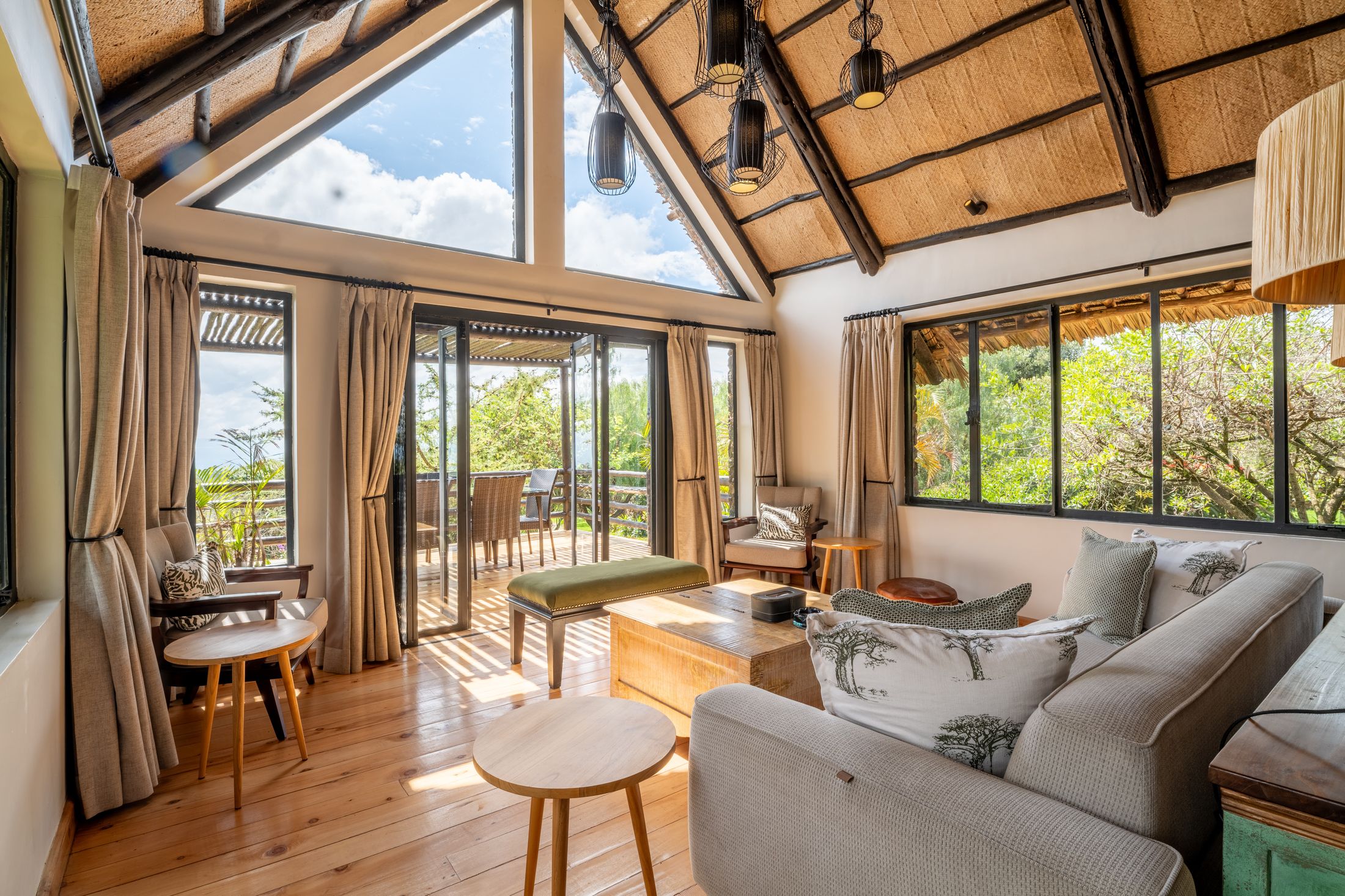 O'Lorien's sitting room under the A-frame thatch, the triangular skylight full of cloud, glass doors open to the deck.