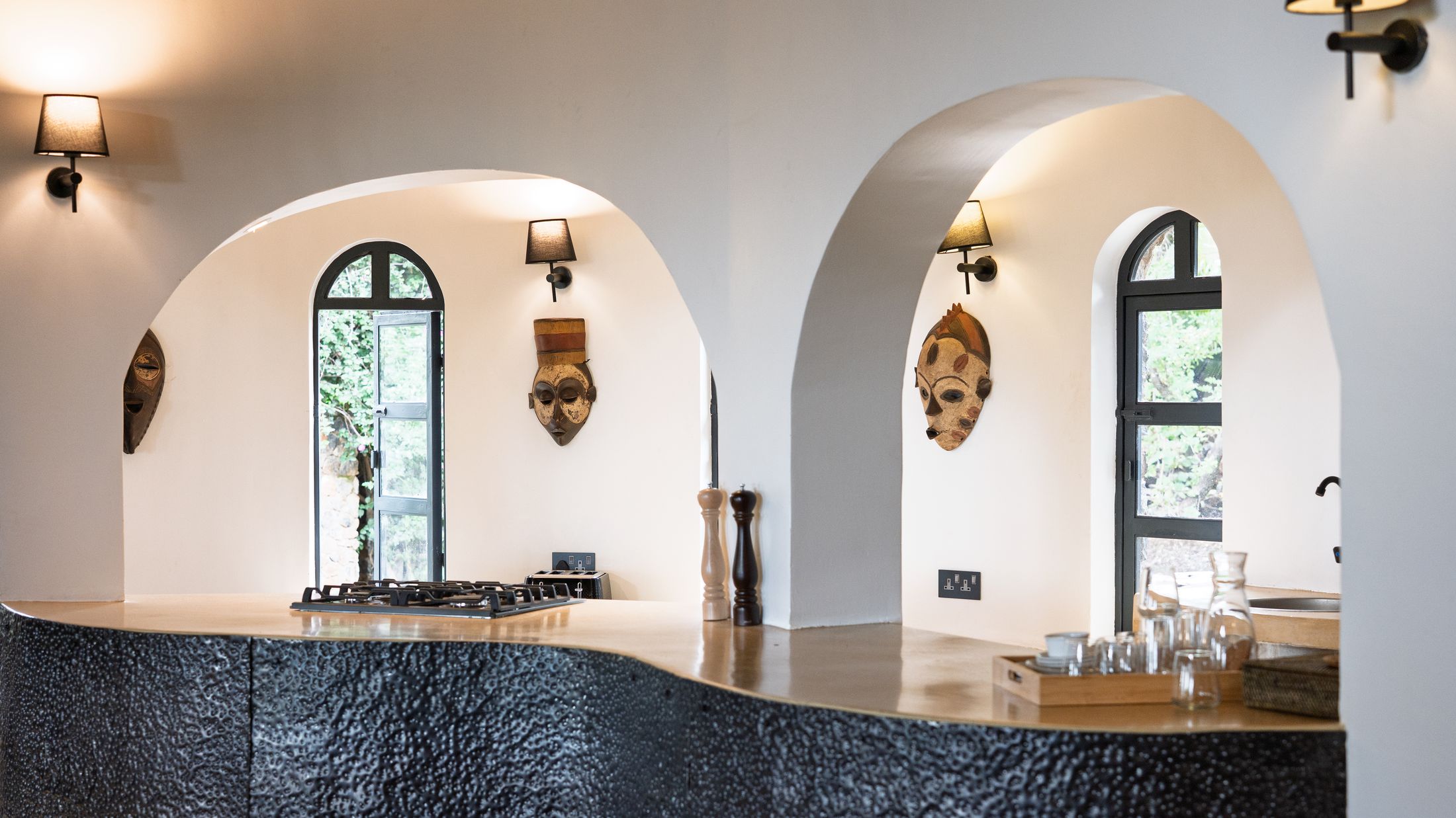 The show kitchen's sculpted black counter beneath twin plaster arches holding carved masks, arched glazed doors to the garden beyond.