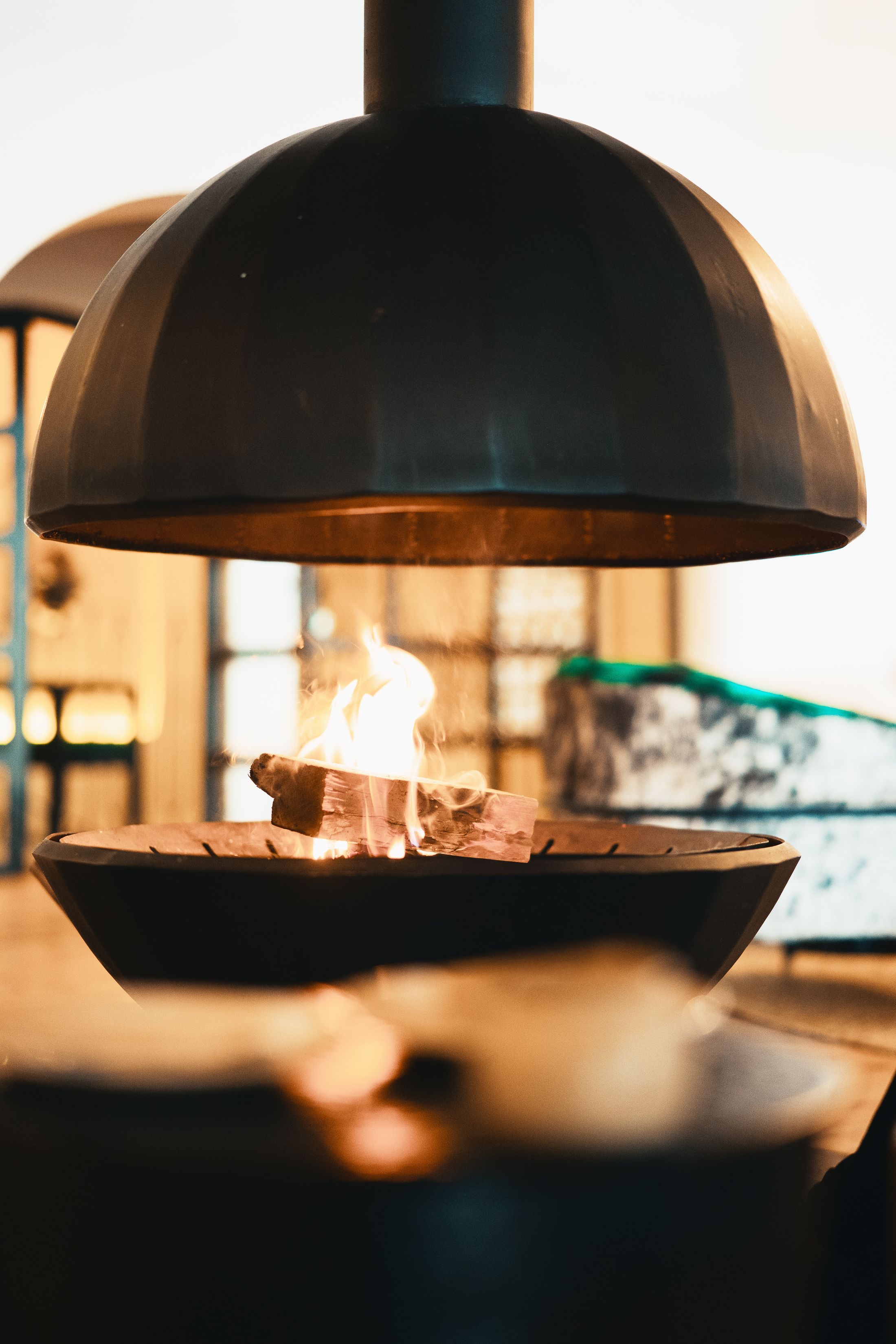 The suspended black cone fireplace at close range, a log burning in the open fire bowl beneath it.